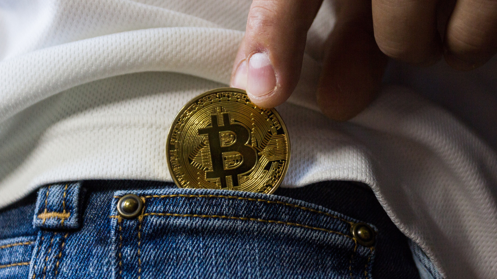 Persona introduce una moneda bitcoin en el bolsillo de pantalón